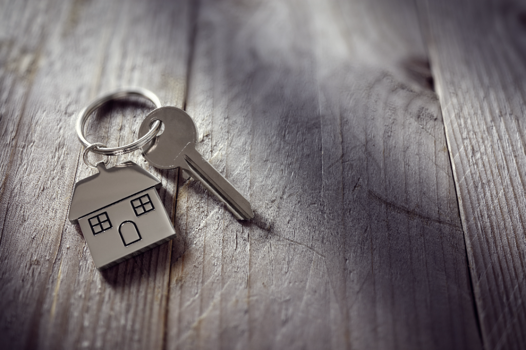 House key with house-shaped keyring on a wooden surface
